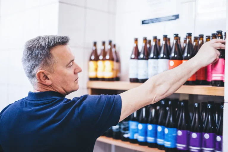 Man arranging custom beer bottles with functional labels on a store shelf.